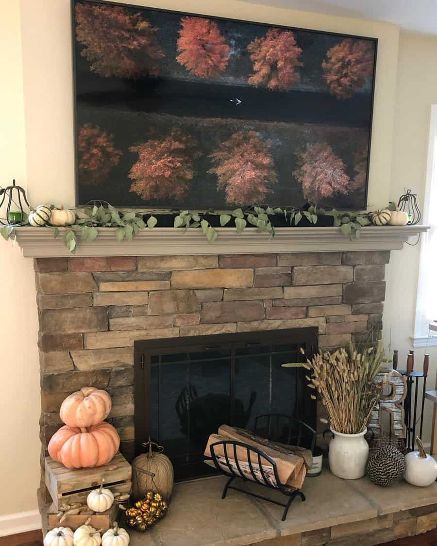 A stone fireplace with a TV above showing autumn trees; pumpkins and greenery decorate the mantel and hearth