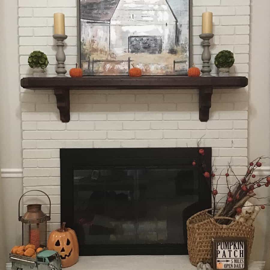 White brick fireplace with a shelf, painting, candles, and small pumpkins; decor includes basket, lantern, carved pumpkin, and sign