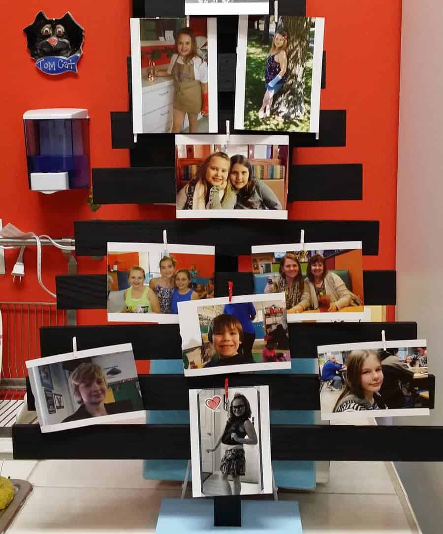 Photo display stand with multiple pictures of children in a room with orange walls and various objects in the background