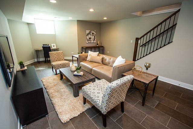 Modern basement family room with a neutral color palette, cozy seating, tiled flooring, and a workspace for a functional and stylish space.