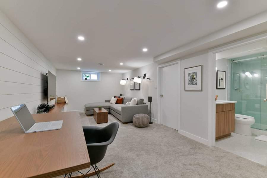 Modern basement with a cozy living area, home office space, shiplap accent wall, and an en-suite bathroom for a functional and stylish retreat.