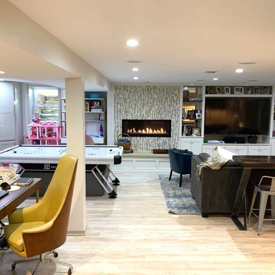 Cozy and multifunctional basement with a fireplace, built-in entertainment center, air hockey table, and workspace for family fun and relaxation.