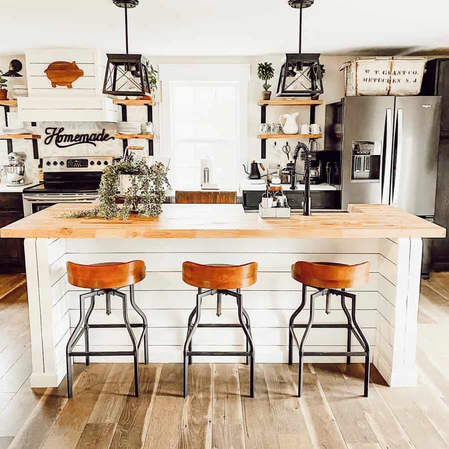 Bright farmhouse breakfast bar with a white shiplap island, warm wood countertops, leather barstools, open shelving, and rustic lantern lighting