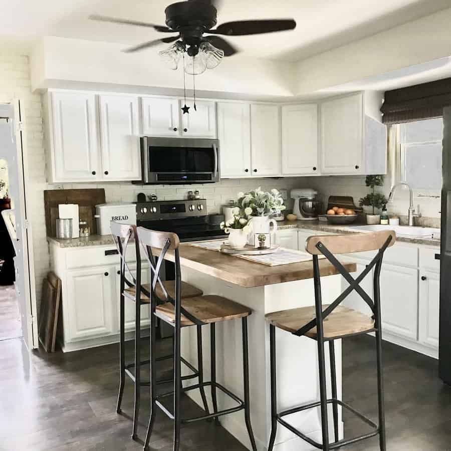 Cozy farmhouse kitchen with a white island breakfast bar, wooden countertop, black metal barstools, and rustic decor for a warm, inviting feel