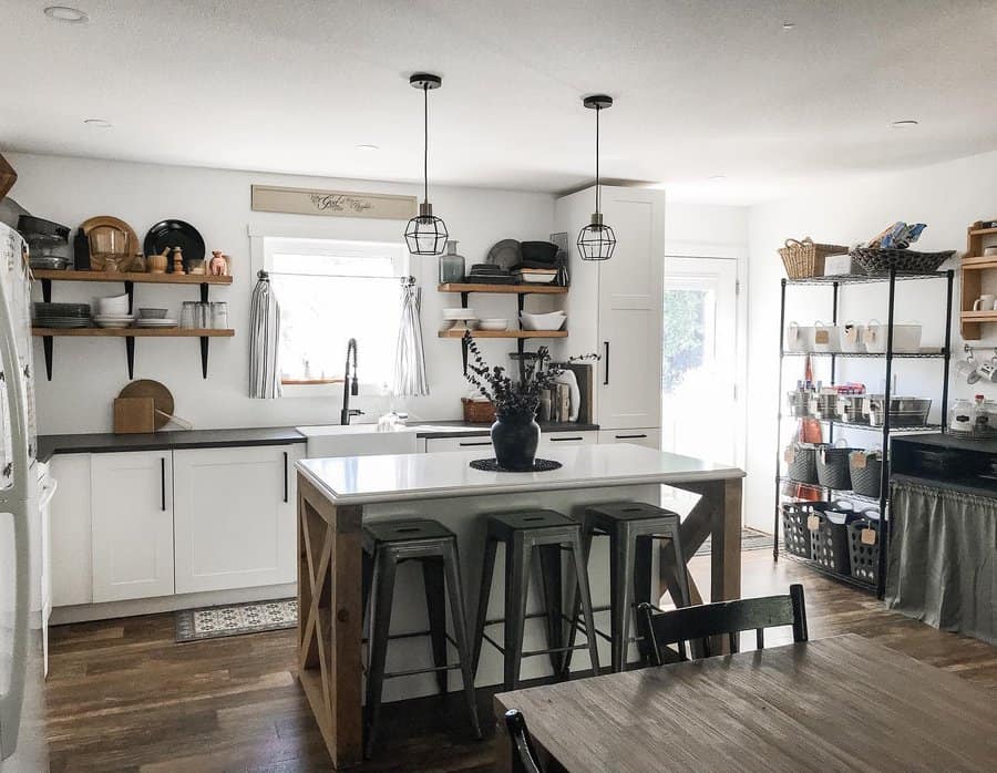 Rustic farmhouse kitchen with a white island breakfast bar, wooden accents, industrial barstools, open shelving, and black pendant lighting