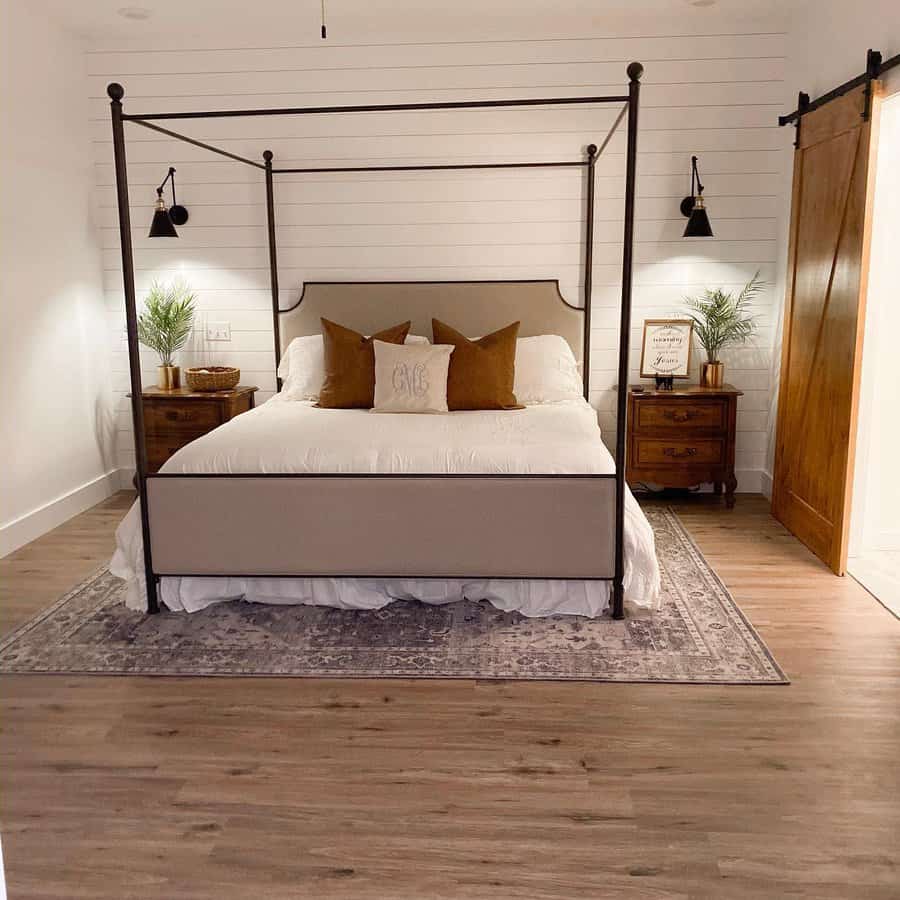 Farmhouse canopy bed with a black metal frame, neutral bedding, warm-toned pillows, shiplap walls, and rustic wood accents for a cozy retreat