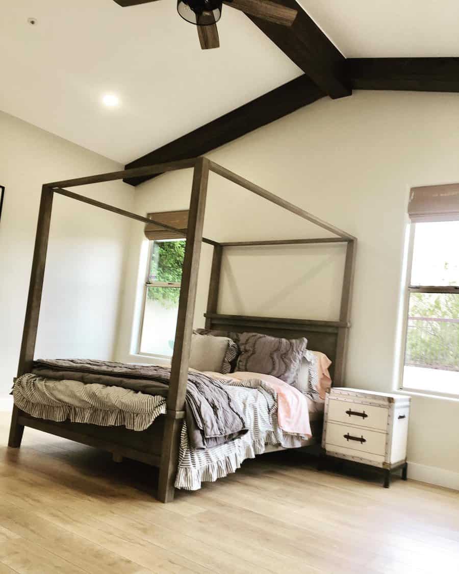 Bedroom with a wooden canopy bed, striped bedding, and a rustic nightstand, featuring wooden beams on the ceiling and a visible ceiling fan