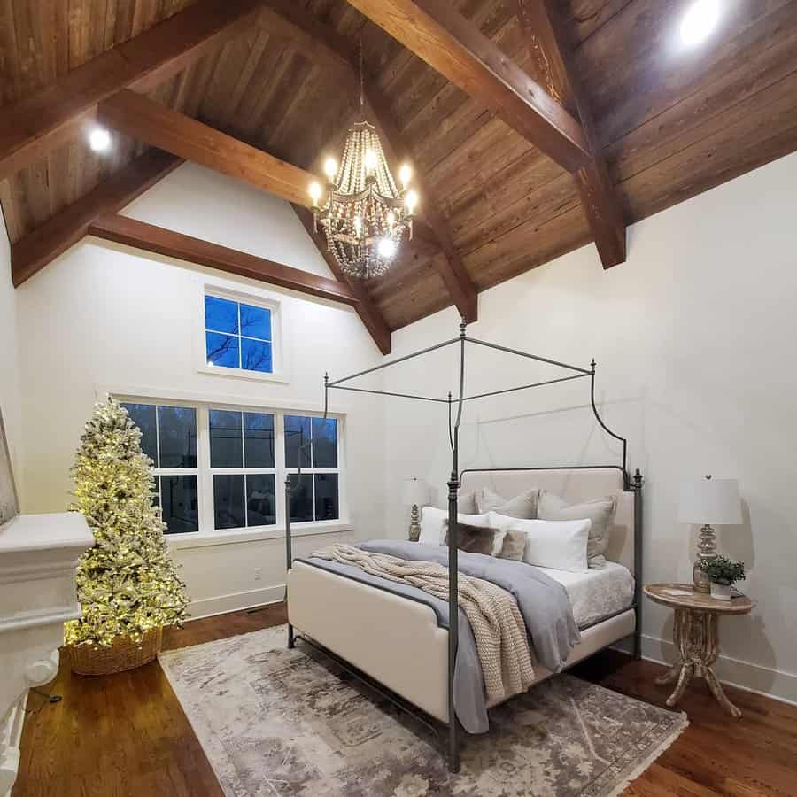 Cozy bedroom with a high wooden ceiling, canopy bed, elegant chandelier, and a decorated Christmas tree by the window