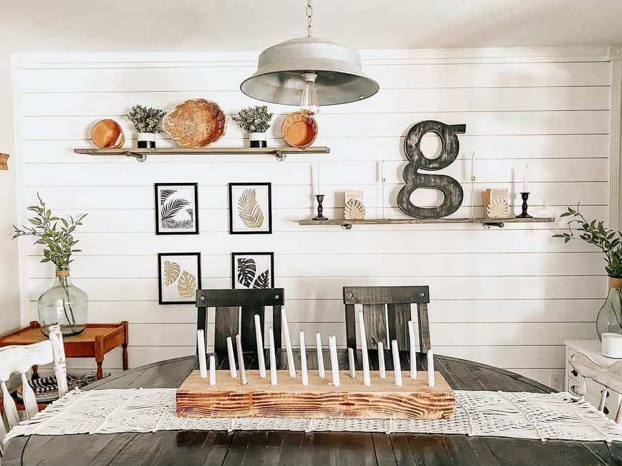 A dining room with a farmhouse style table, candle centerpiece, and wall shelves with decor, including a large metal letter "g"