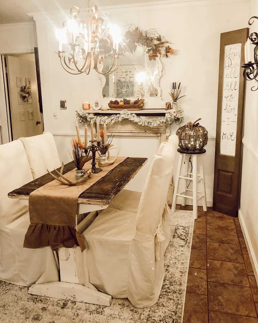 Cozy dining room with a rustic wooden table, white slipcovered chairs, chandelier, and autumn-themed decorations