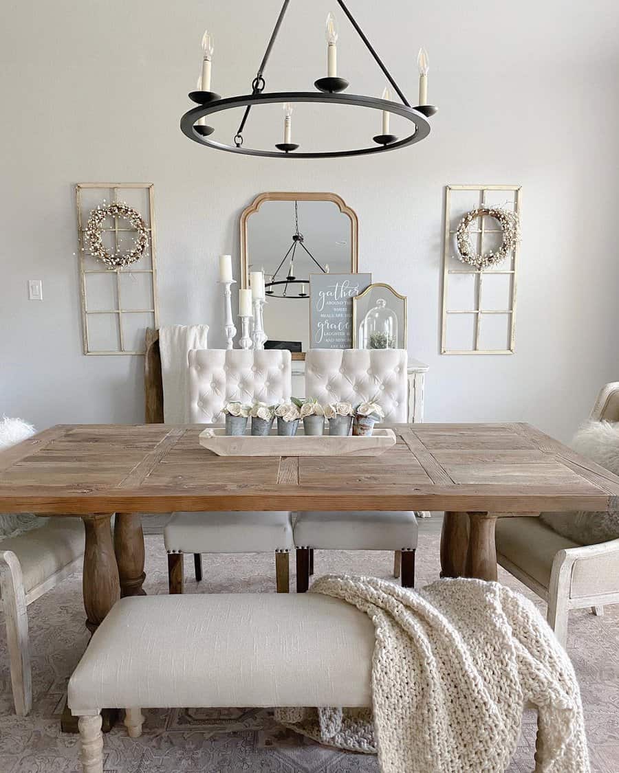 Dining room with a wooden table, beige chairs, and a soft throw blanket; decor includes candles, a mirror, and rustic wreaths