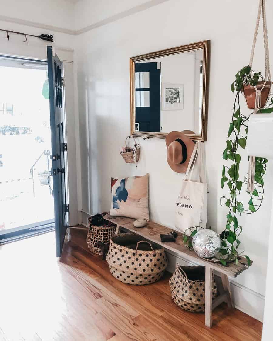 Boho farmhouse entryway with a rustic wooden bench, woven baskets, a gold-framed mirror, and greenery, creating a relaxed and stylish vibe