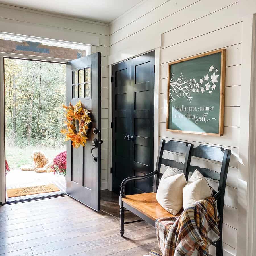 Cozy farmhouse entryway with a black and wood bench, autumn decor, shiplap walls, and a welcoming wreath, creating a warm seasonal charm