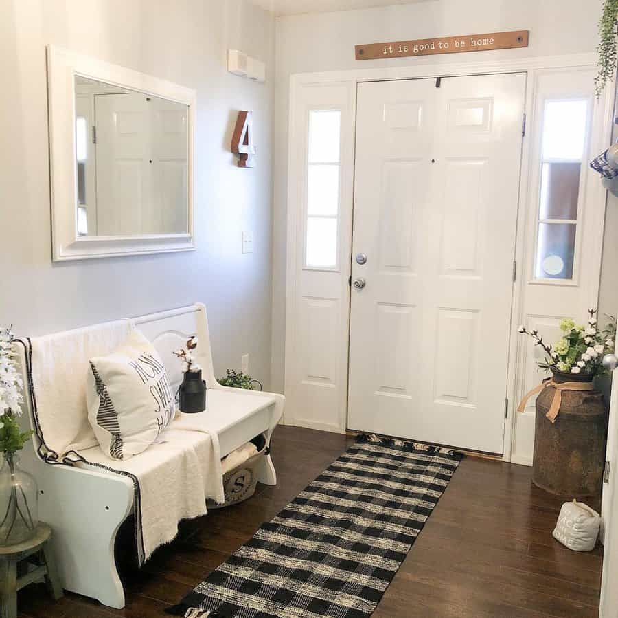 Bright farmhouse entryway with a white bench, cozy throw pillows, rustic accents, and a checkered runner, creating a welcoming and charming space