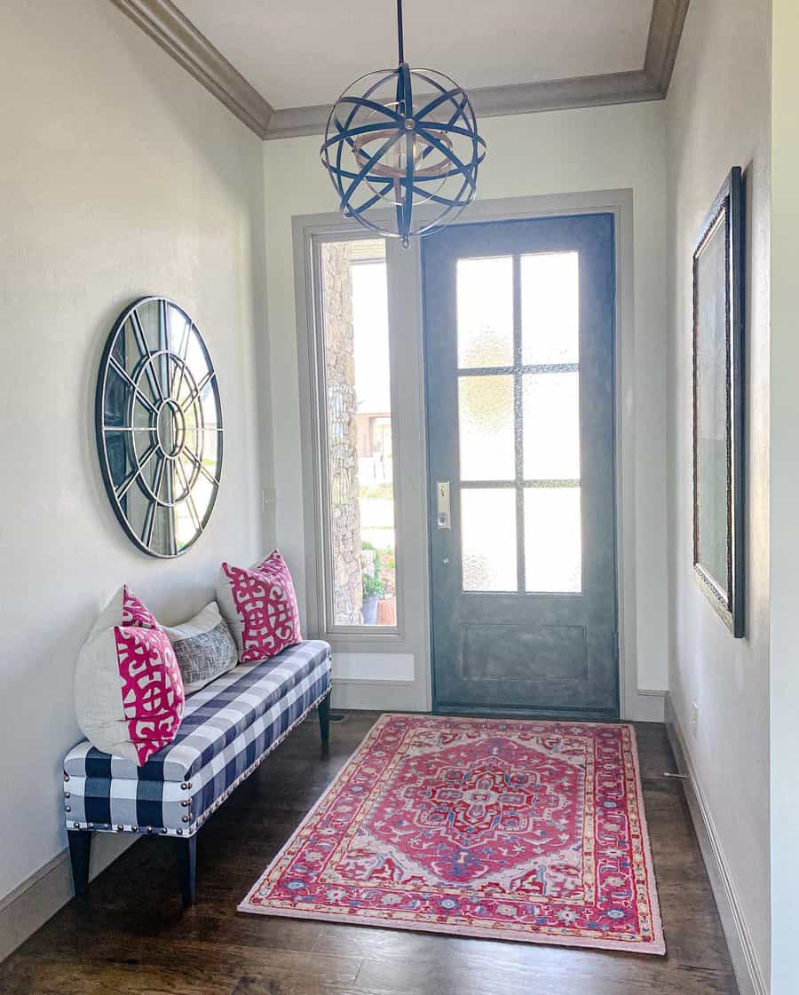 Hallway with a checkered bench, pink pillows, round mirror, and a colorful rug under a geometric pendant light by the front door