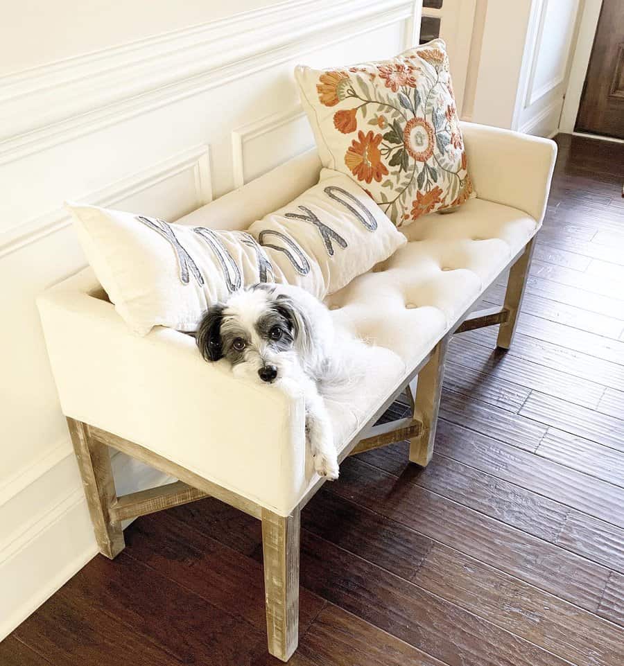 Elegant farmhouse entryway with a tufted bench, embroidered pillows, and a cozy pup, creating a warm and inviting space with rustic charm