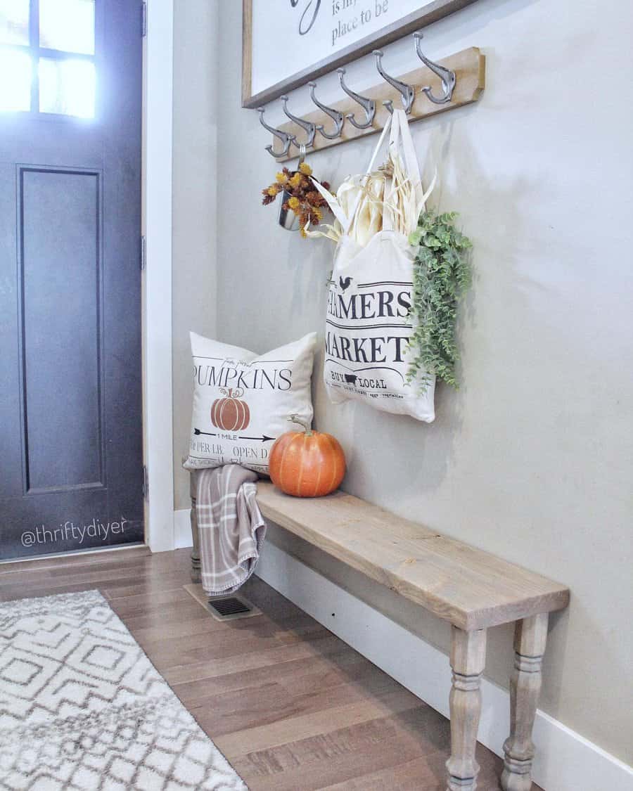 Cozy entryway with a wooden bench, pillows, fall decor, a small pumpkin, and hanging bags on hooks