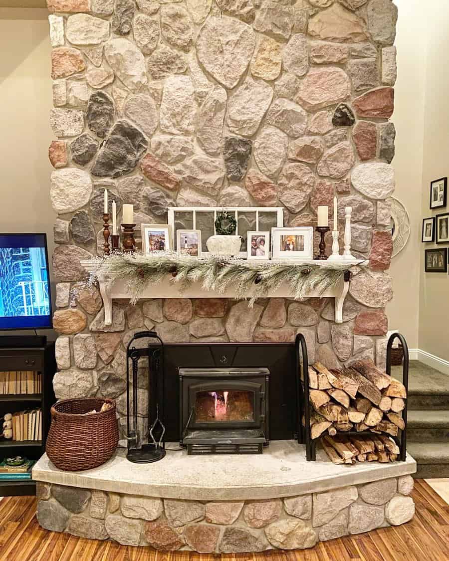 Stone fireplace with lit fire, decorated mantel with candles, garland, and framed photos; firewood stacked on the right, TV on the left