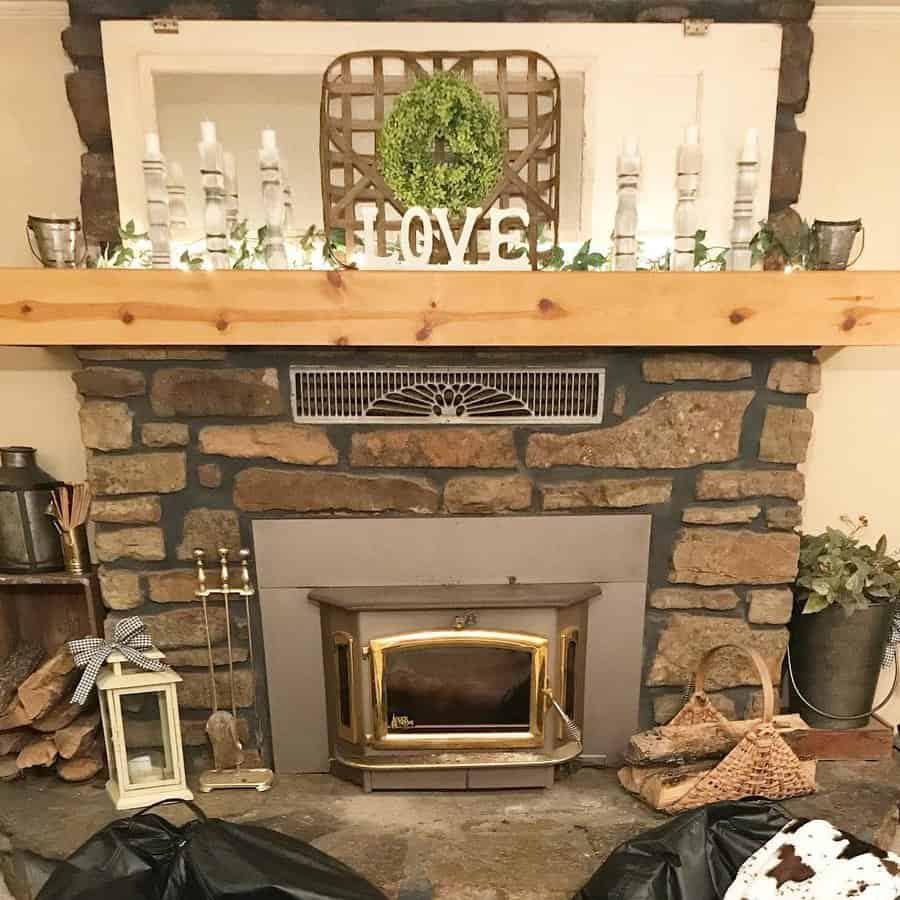 Stone fireplace with wood stove, decorated mantel with candles, plants, a "LOVE" sign, and a wreath above