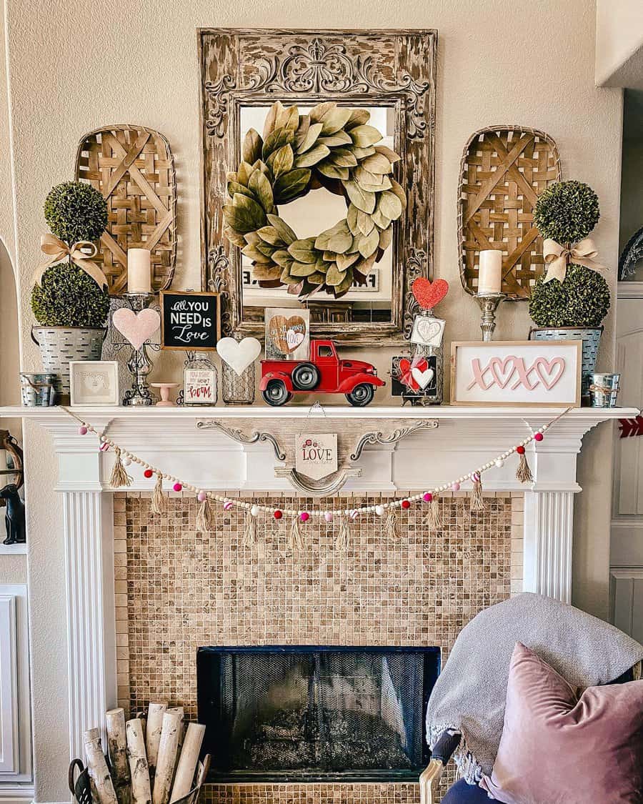 Cozy decorated mantel with a wreath, candles, topiaries, a red toy truck, heart ornaments, and garlands over a mosaic-tiled fireplace