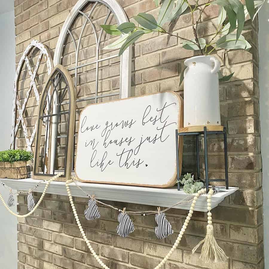 A rustic brick wall display with arch mirrors, potted greenery, a vase, and a sign reading "love grows best in houses just like this"