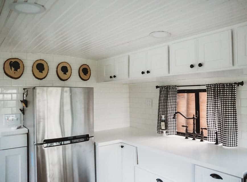 Rustic farmhouse kitchen with a white countertop, black vintage faucet, gingham curtains, and wooden silhouette wall art for a cozy charm