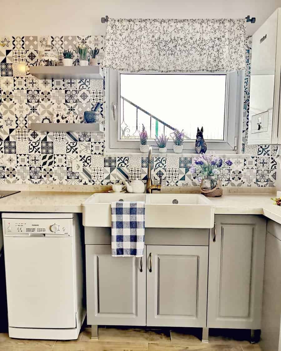 Small kitchen with patterned tile backsplash, white farmhouse sink, gray cabinets, and a window with floral curtains