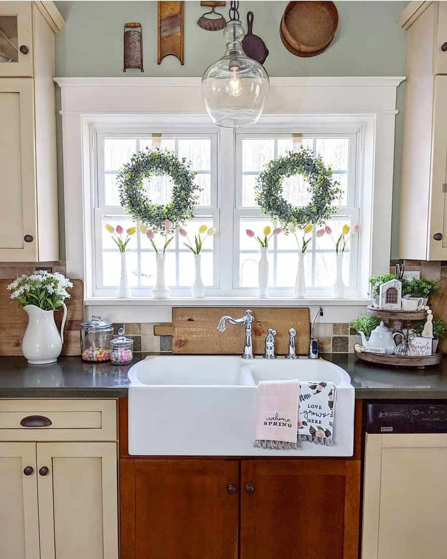 A cozy kitchen with a farmhouse sink, wreath-adorned window, and tulips in vases, light cabinets and rustic decor accent the space