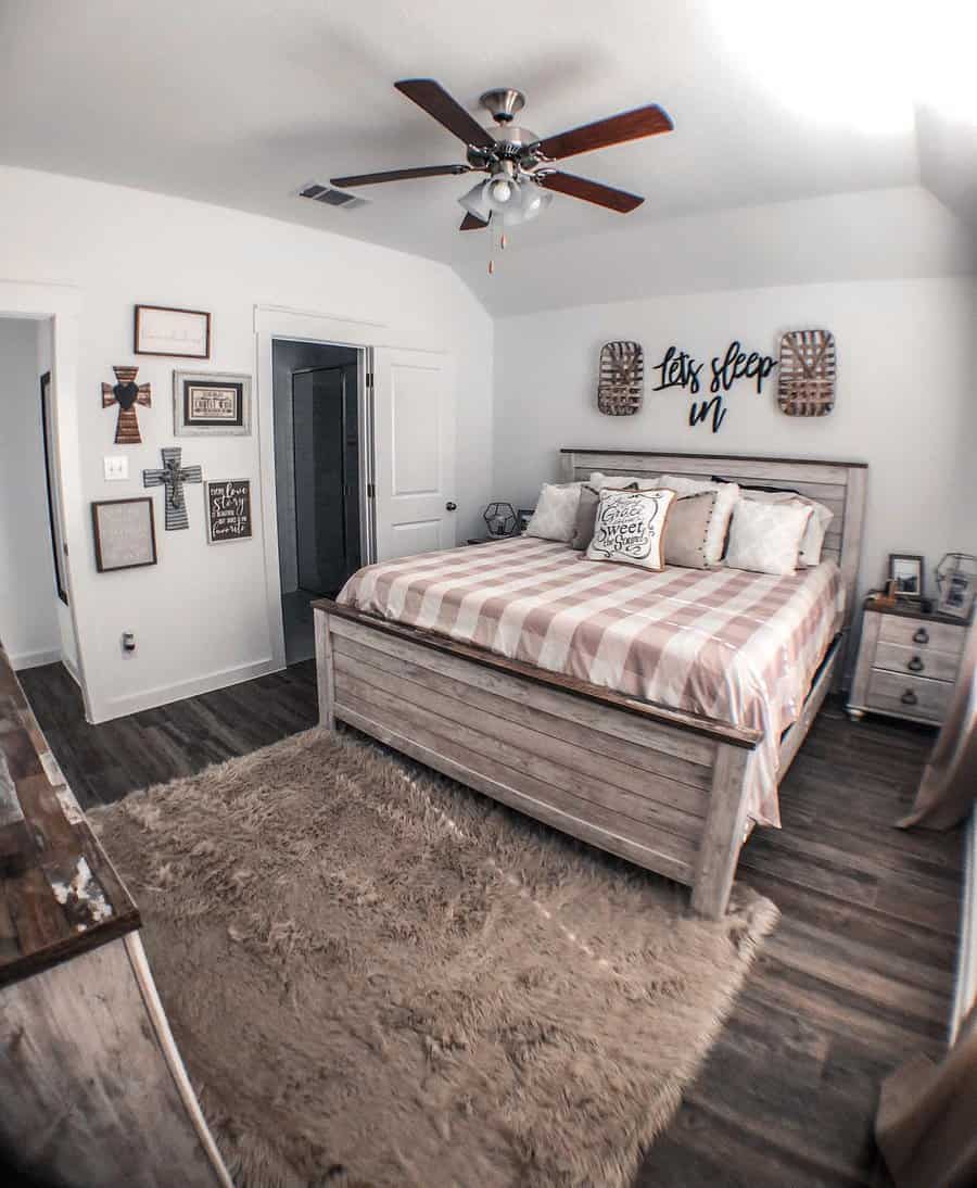 Cozy bedroom with a wooden bed, striped bedding, wall decor, ceiling fan, and a shaggy rug on wooden flooring