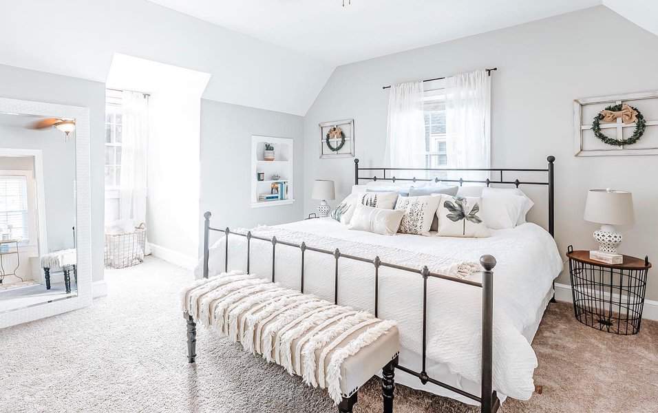 Bright farmhouse-style master bedroom with an iron bed frame, cozy neutral decor, and soft natural light, creating a warm and inviting retreat