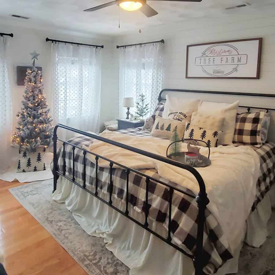 Cozy bedroom with Christmas decor, featuring a plaid bedding, small lit tree, and a "Tree Farm" sign above the bed