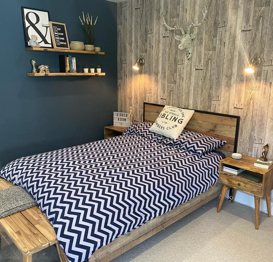 Cozy bedroom with chevron-patterned bedding, wood-accented walls, and decorative items on shelves, warm lighting and rustic wooden furniture