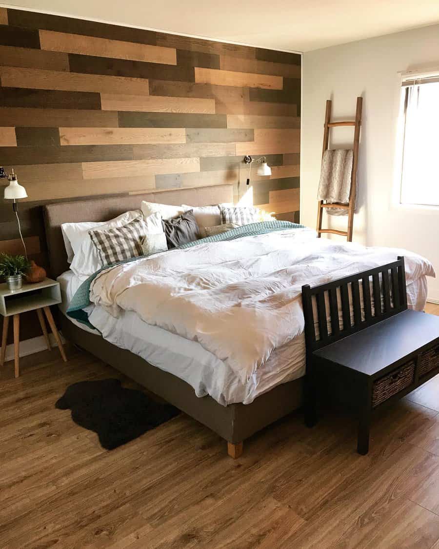 Bedroom with a wood accent wall, cozy bed, checkered pillows, side table with plants, ladder shelf, and bench at the foot of the bed