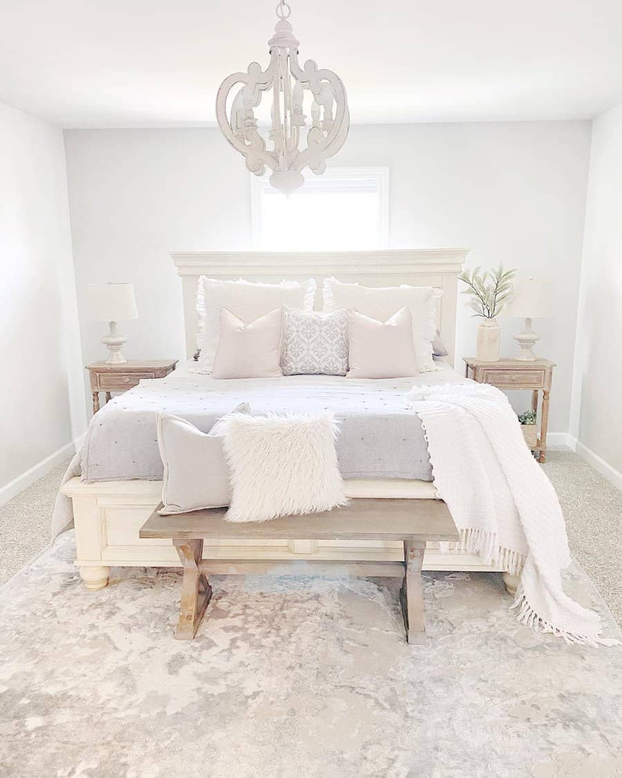 Bright bedroom with a large bed, wooden nightstands, soft pillows, a rustic chandelier, and a decorative bench on a textured rug