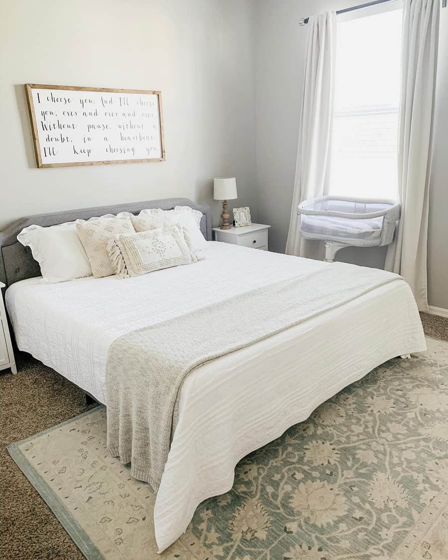 Bright farmhouse-style master bedroom with soft neutrals, cozy bedding, and rustic wall art, creating a warm and inviting atmosphere