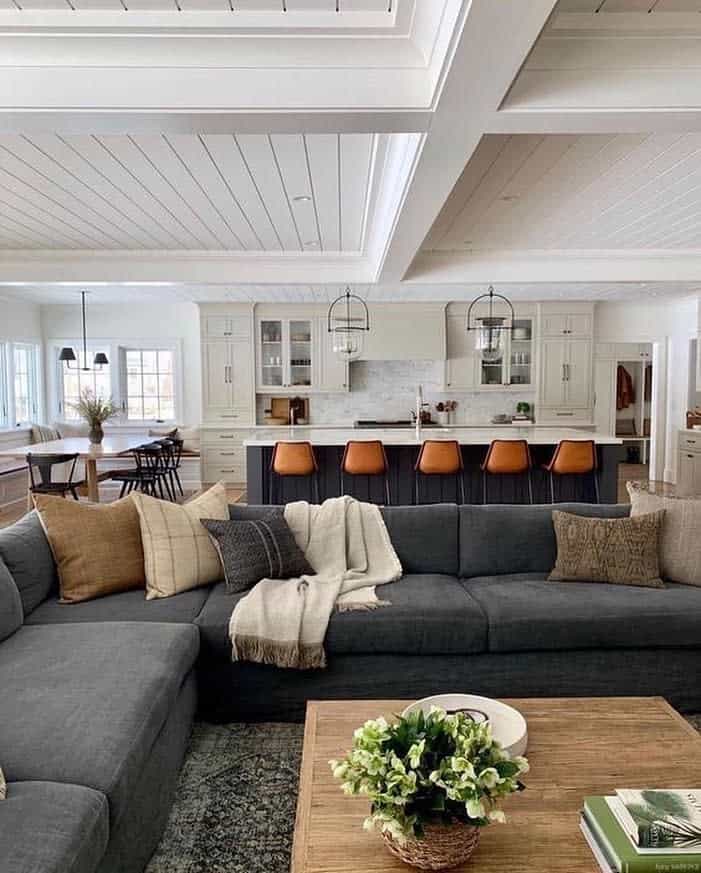 Open-plan living area with a gray sectional sofa, wood coffee table, kitchen island with orange stools, and dining table in the background