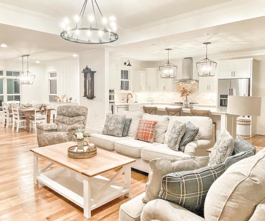 Open-concept living and dining area with light beige sofas, wooden coffee table, pendant lighting, and a modern kitchen in the background