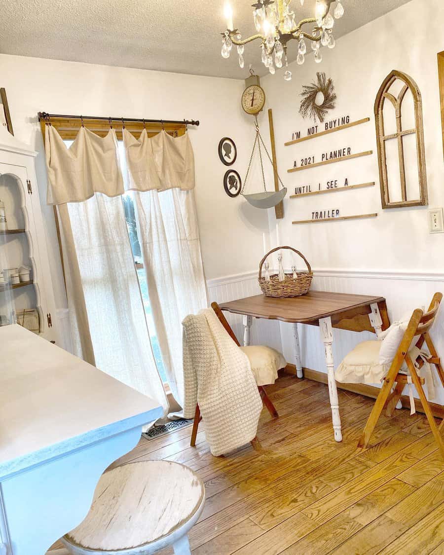 Cozy dining area with wooden floors, a small table, wicker basket, folding chairs, wall decor, chandelier, and sheer curtains