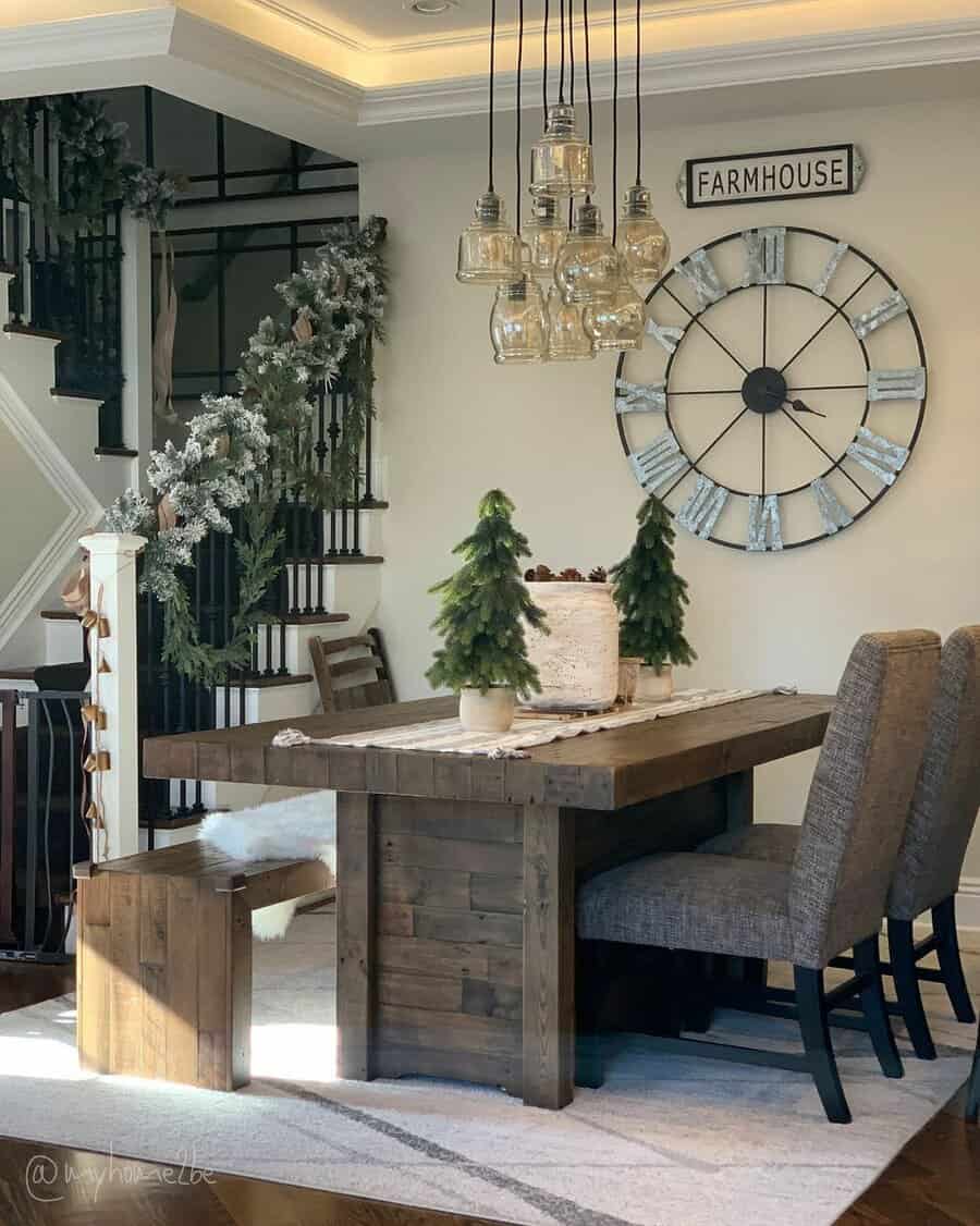 Cozy farmhouse dining area with a wooden table, cake, two small trees, a rustic clock, and a staircase decorated with garland