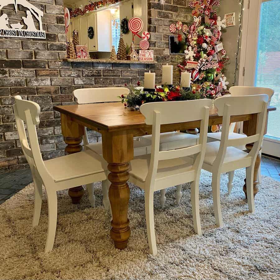 Dining room with a wooden table, white chairs, Christmas tree, festive centerpiece, and brick wall with holiday decor