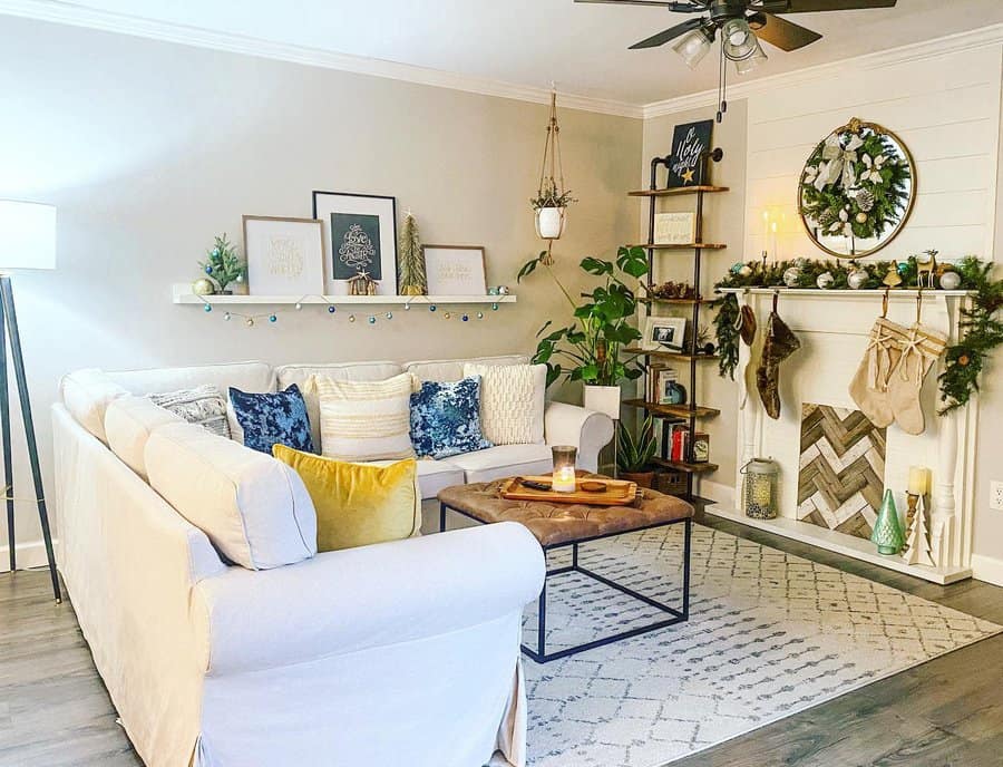 Small living room with a white sectional, decorative pillows, festive mantle with stockings, plants, and wall art under a ceiling fan