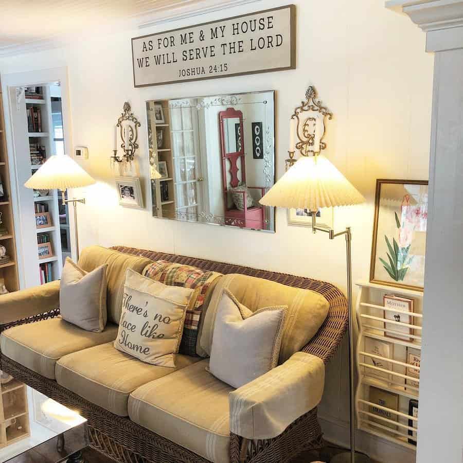 Cozy farmhouse living room with a wicker sofa, warm neutral tones, soft pillows, vintage lighting, and a faith-inspired wall sign for a welcoming feel