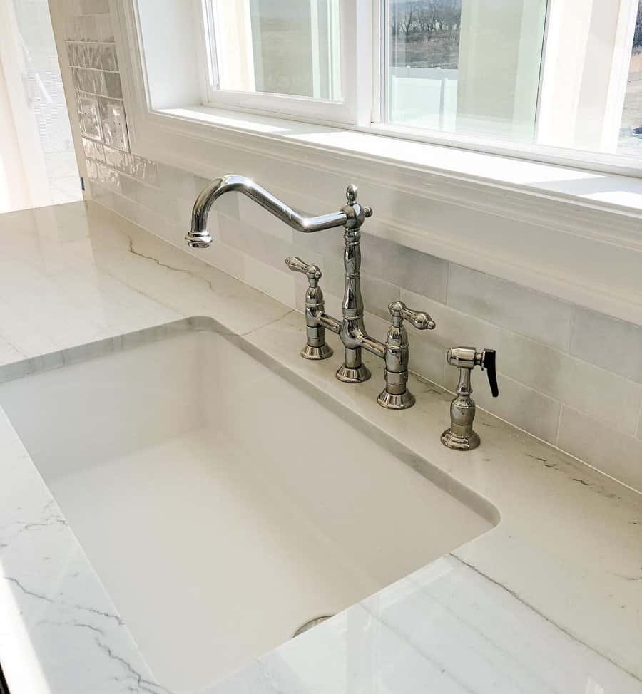 A sleek, modern kitchen sink with a polished, silver faucet and sprayer, white marble countertops, and a light tile backsplash