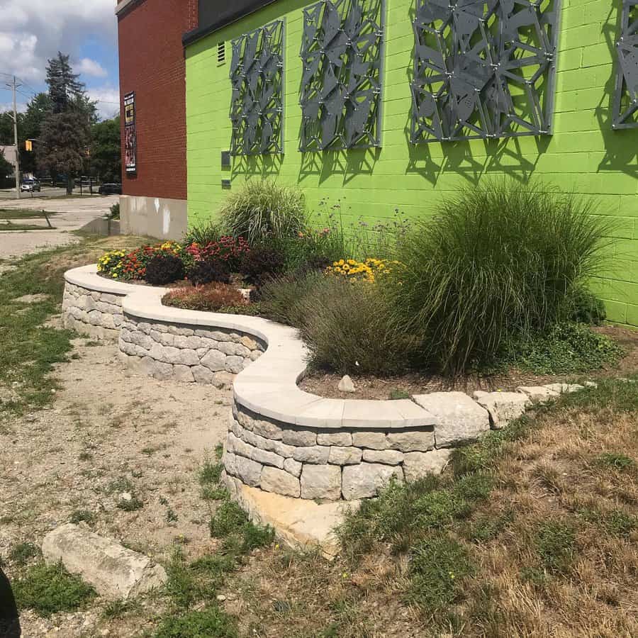 Modern outdoor wall with geometric metal decor on a bright green facade, complemented by a curved stone planter filled with colorful flowers