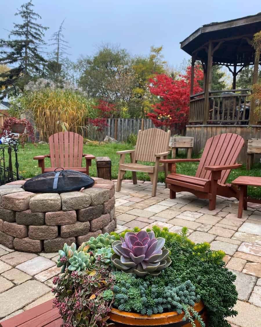 Backyard patio with Adirondack chairs around a stone fire pit, surrounded by colorful foliage and a succulent planter in the foreground