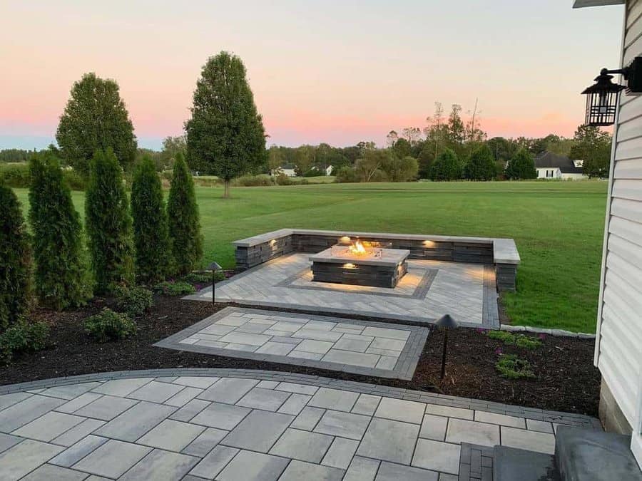 Modern backyard fire pit with sleek stone seating, tiled patio design, and a scenic open field view during sunset