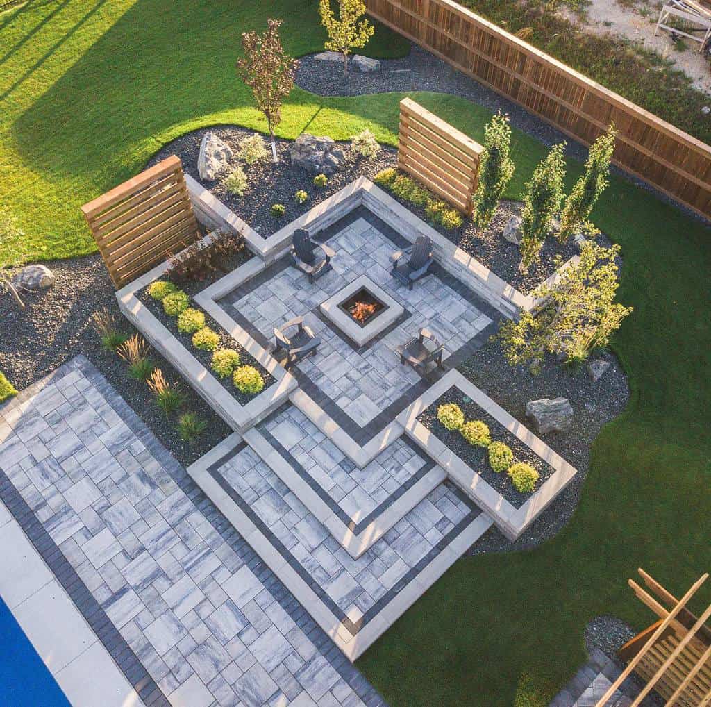 Aerial view of a geometric backyard fire pit design with modern stone seating, lush greenery, and wooden privacy panels