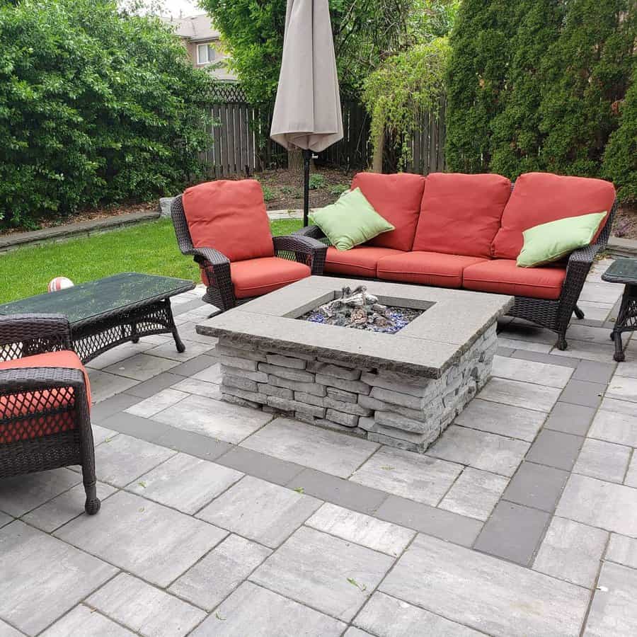 Cozy backyard patio with stylish stone pavers, a modern fire pit, and comfortable wicker seating with red cushions for a warm outdoor retreat