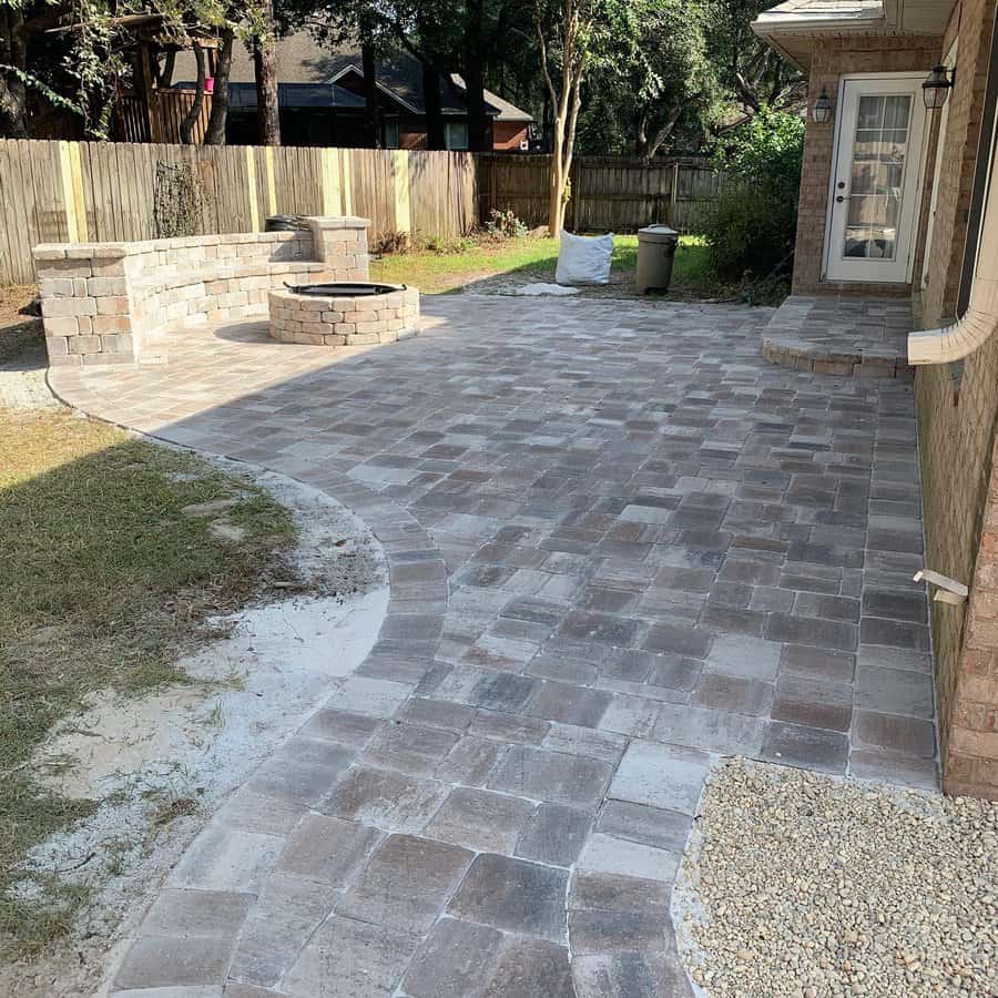 Spacious backyard patio with rustic stone pavers, a built-in fire pit, and a curved seating wall for a functional and inviting outdoor space