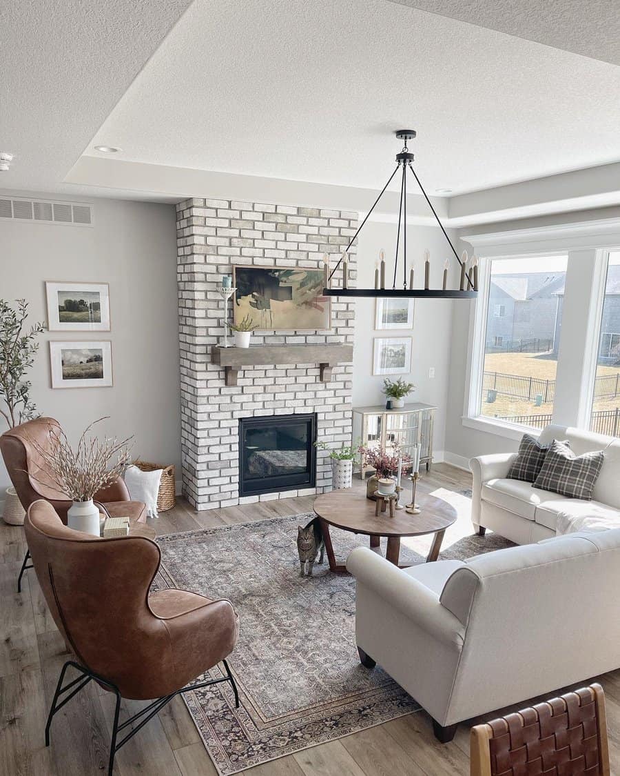 Cozy living room with brick fireplace, armchairs, a coffee table, and large windows